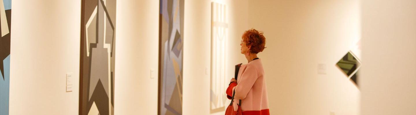 A person standing in a large gallery space looking at a large piece of art on a wall