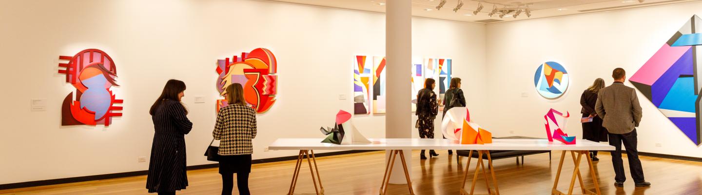 A group of people looking at different art pieces in a large gallery room