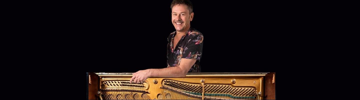 A man smiling while standing behind a piano
