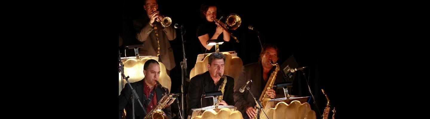 5 musicians playing their brass instruments seated on stage together