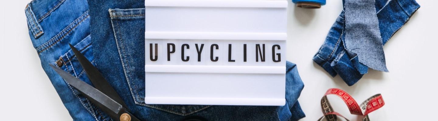 A lgiht up message board that says 'Upcycling', and is surrounded by pairs of jeans with scissors and measuring tape