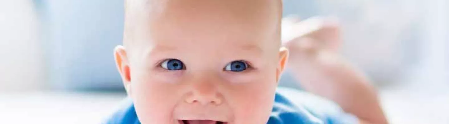 Smiling baby with blue eyes and blue clothing, lying on the stomach.
