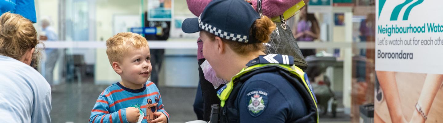 A Victoria Police officer crouches to talk to a young child
