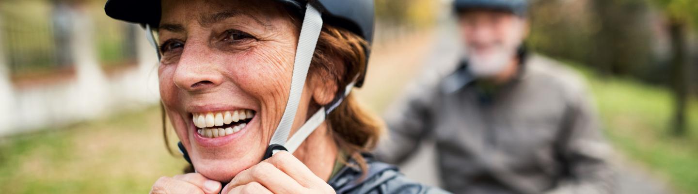 A smiling woman clips on her bike helmet 