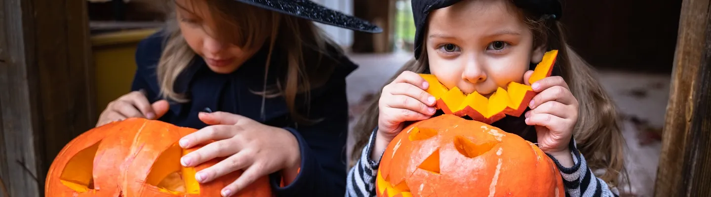Two kids cutting out a face in pumpkins