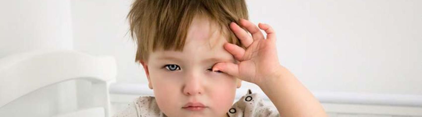 A toddler rubbing their eyes looking tired while standing in a cot