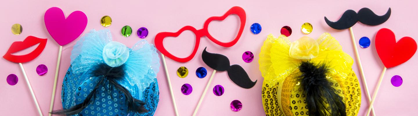 Glitter, feathers, love hearts on sticks and fake moustaches decorate a pink surface
