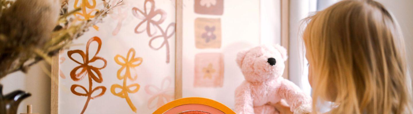 young girl and teddy bear in a childs bedroom. There are hand drawn flowers on the wall.