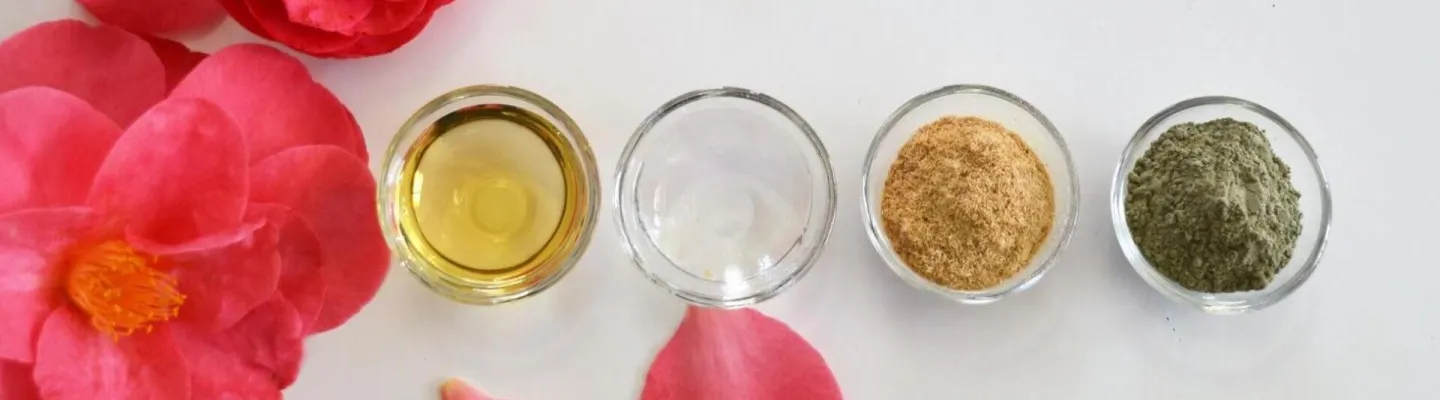 4 small bowls of liquids and powders sitting among pink rose petals 