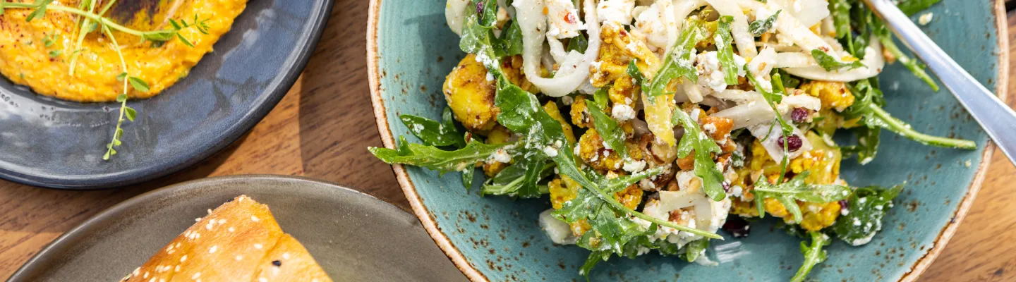 3 plates of food, a pasta dish with rocket and cauliflower, bread, and a bowl of dip.