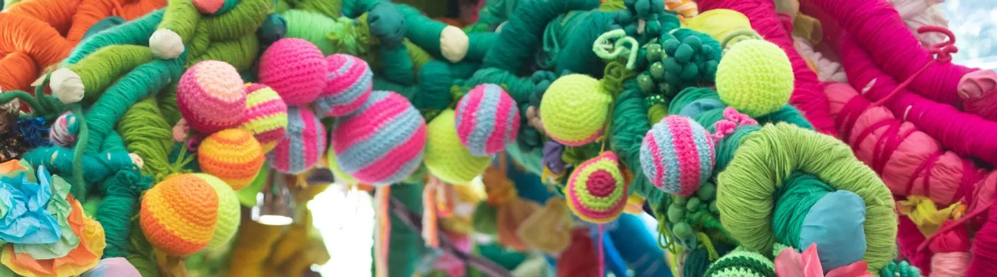 image of sculptural artwork featuring brightly coloured knitted balls and pink and green knitted vines