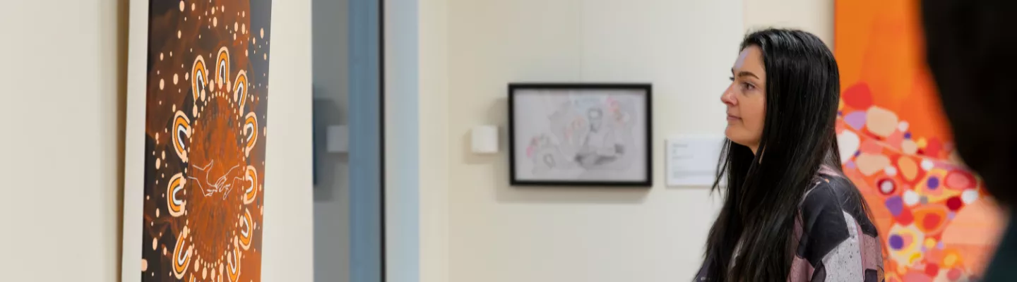 Photograph of a person with long dark hair looking at artworks in a gallery