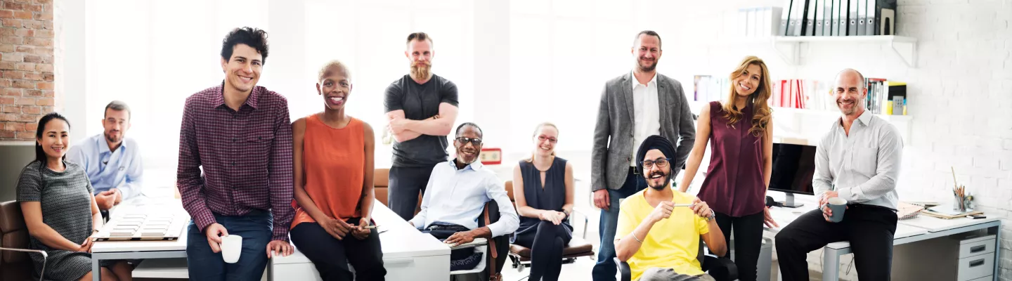 a diverse group of people sitting and standing at desks