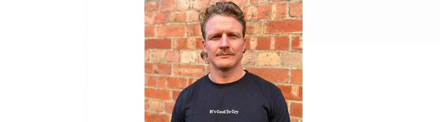 Headshot of a young man in a black t-shirt that says it's cool to cry