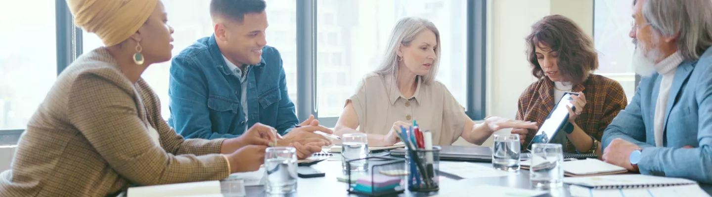 Group of people sitting around a table having a discussion in a bright room with big windows