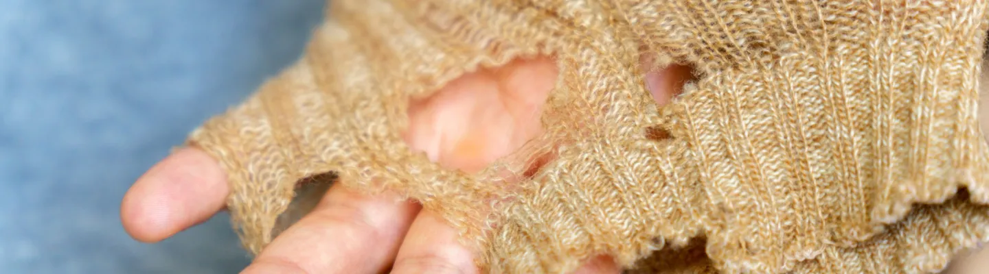 An arm wearing a woollen beige jumper with big holes 