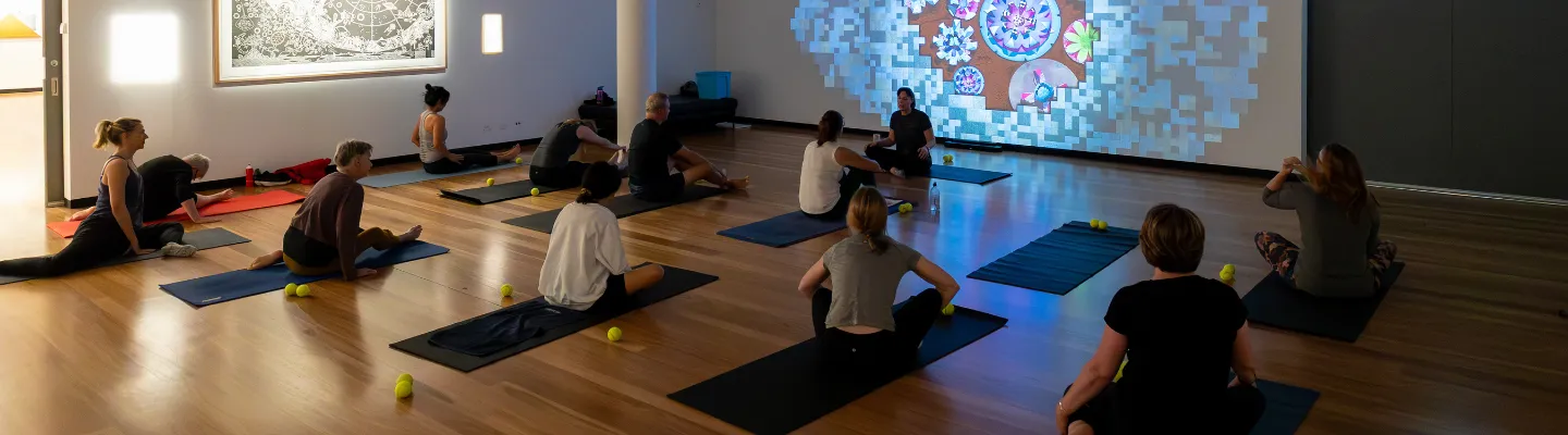 Group of participants doing pilates on yoga mats in a dimly lit gallery
