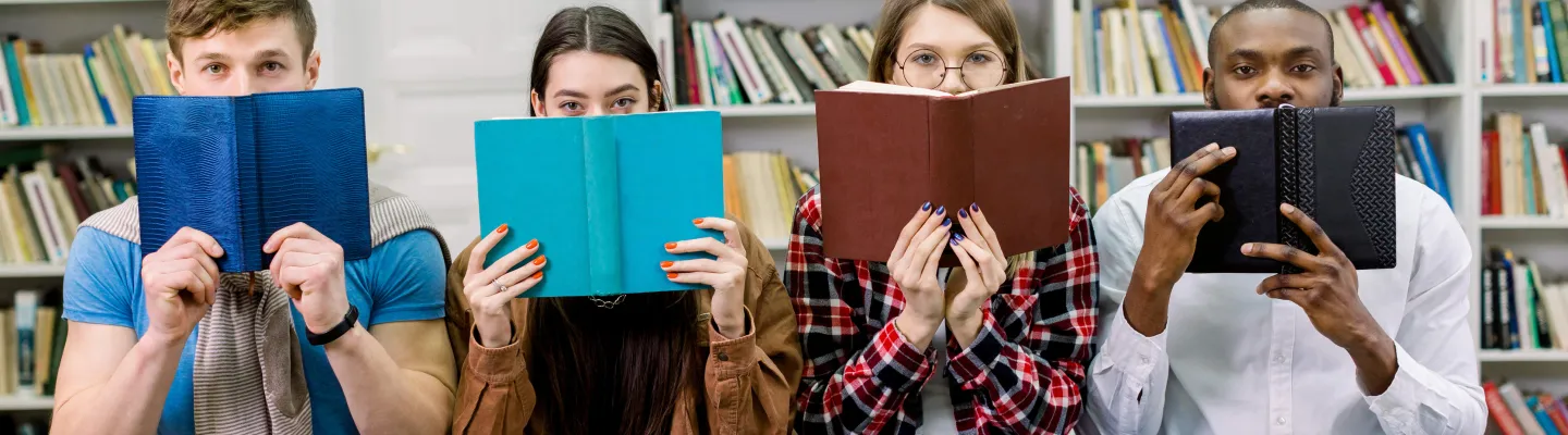 Four people holding books in a library