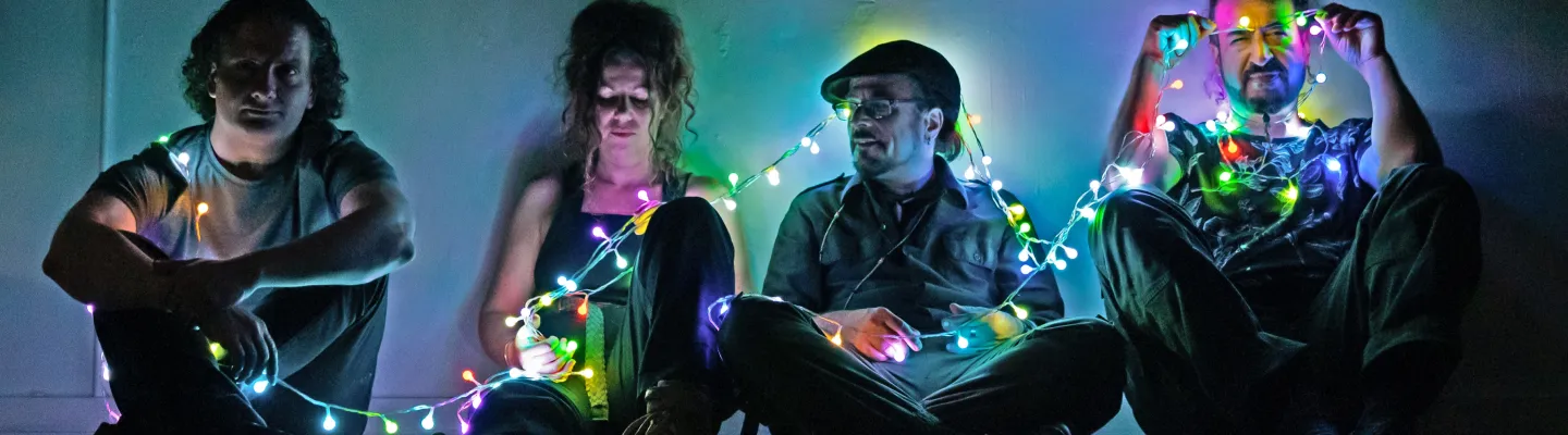 The four members of Bashka sit together in a house, a string of colourful fairy lights connecting them..