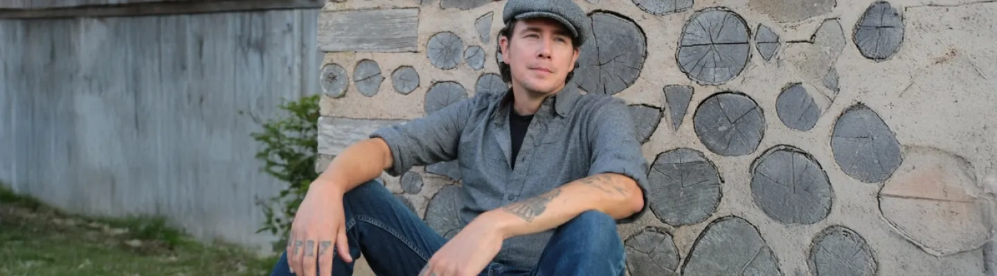 A man in a peaked cap sits back against a stone wall