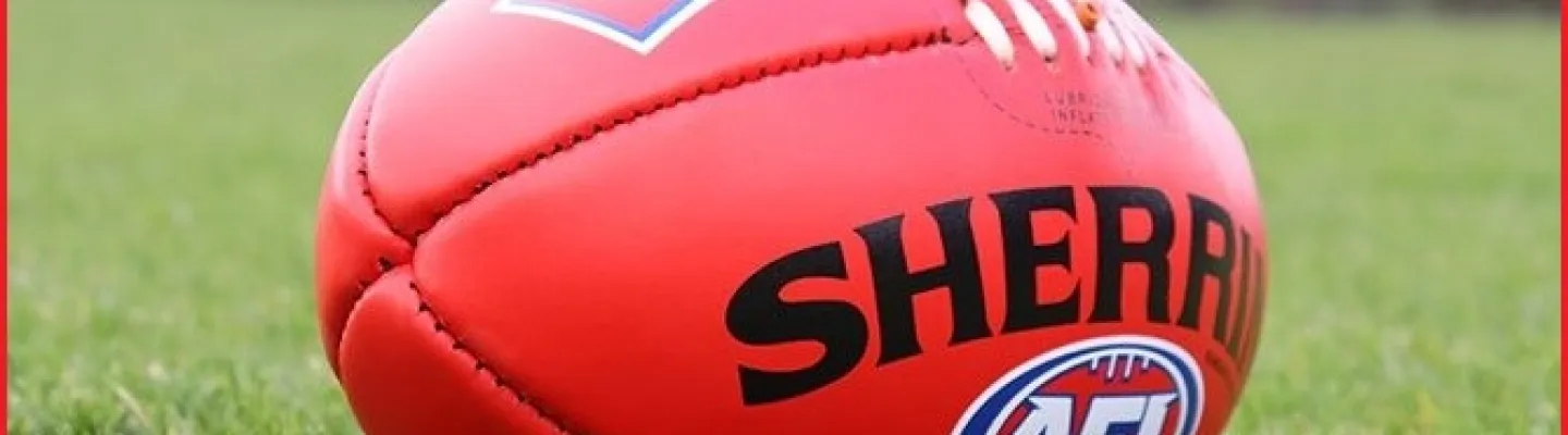 A red football with logos lies on a grassy field.