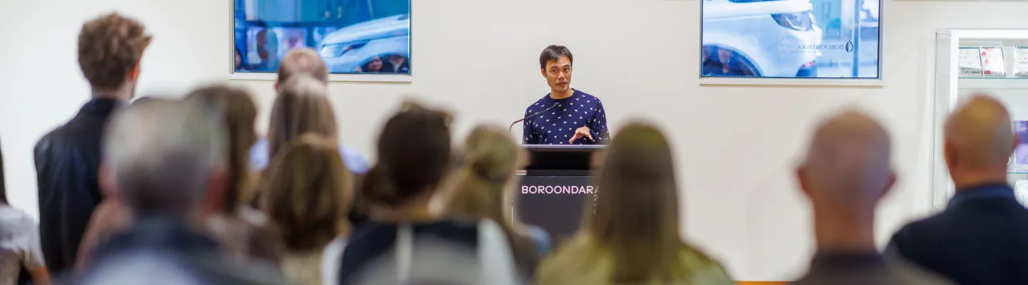 Crowd of people facing an artist speaking at a lectern.