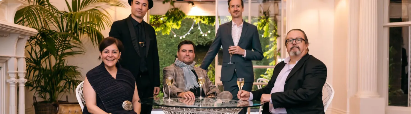 5 well-dressed adults sit at a wicker dinner setting