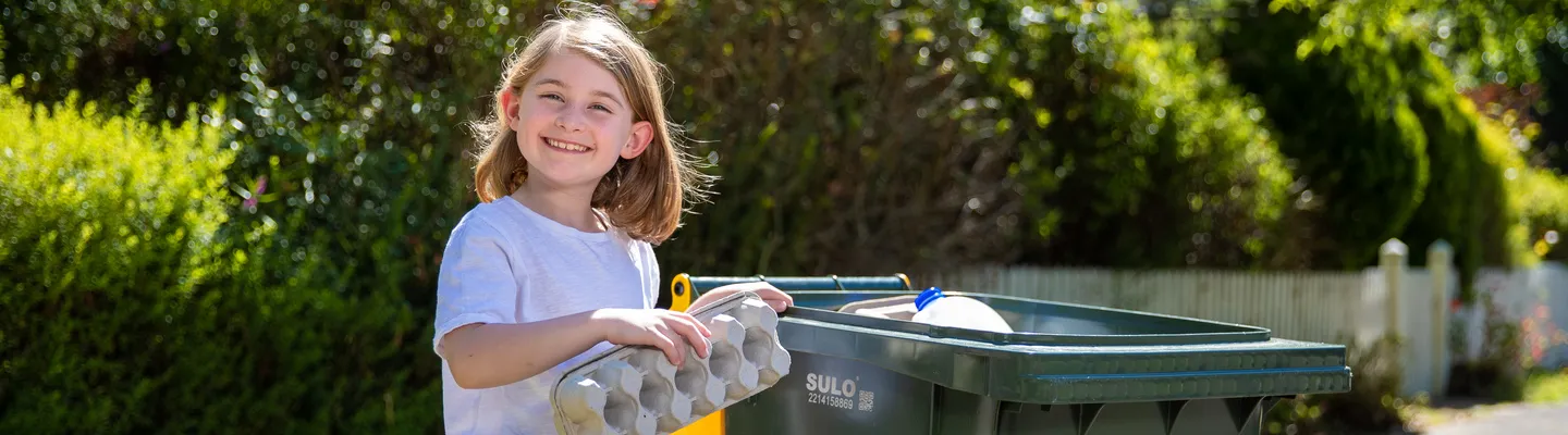 child putting an egg carton in the recycling bin