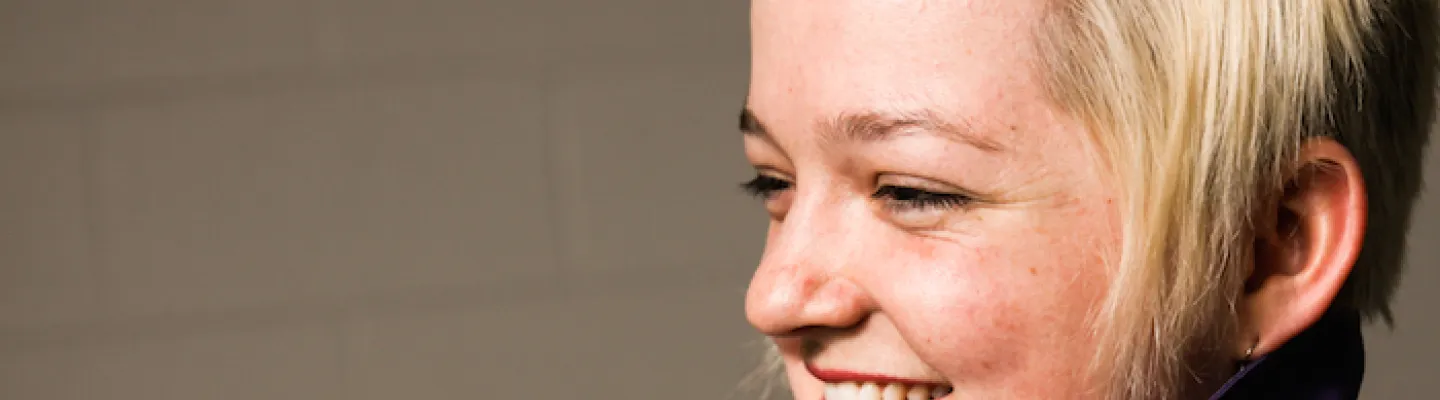 Close up side profile of person smiling and looking away. They have short blond hair.