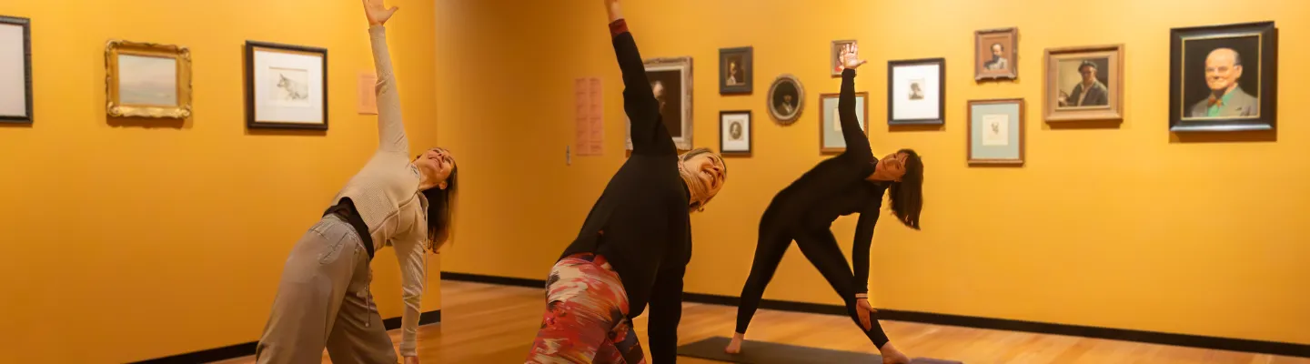 3 women on yoga mats stretching with one arm up in the air and the other on their legs
