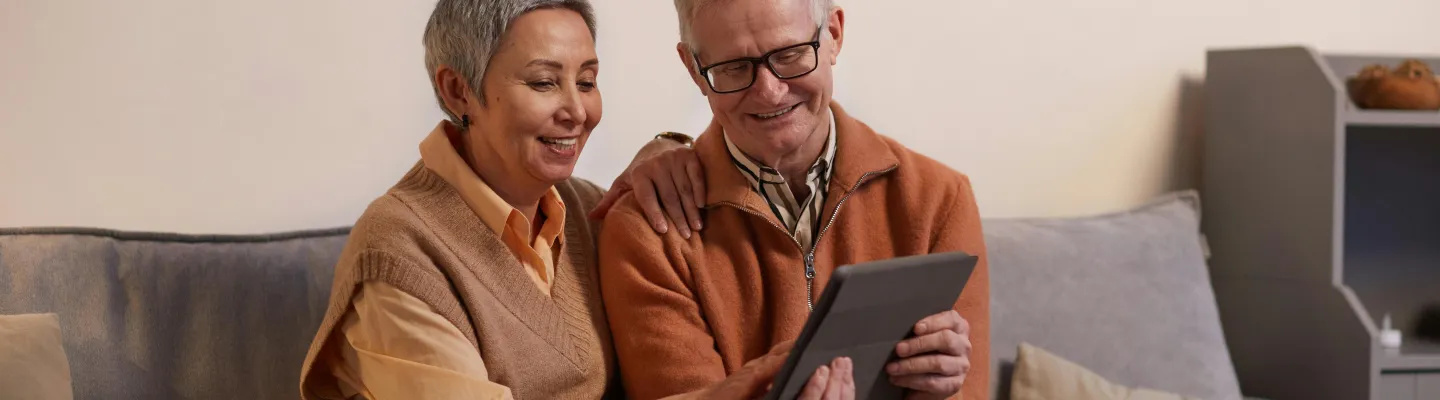Man and Woman Sitting on Sofa While Looking at a Tablet Computer