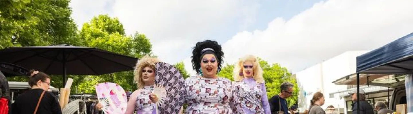 Three women wearing makeup smiling together at an outdoor event.