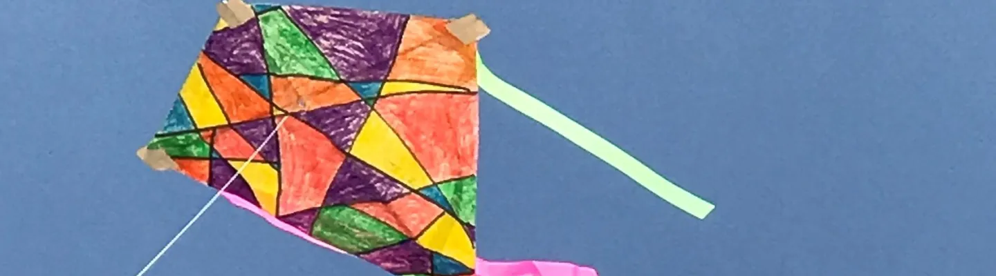 A colourful kite with streamers is flying on a blue background.