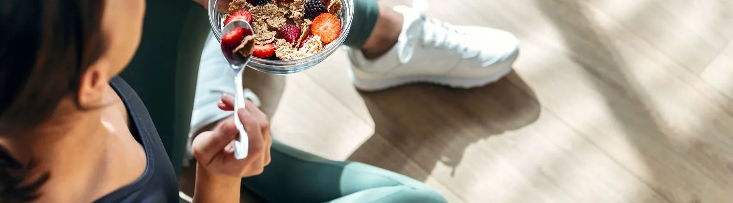 A woman in activewear eating a breakfast bowl of fruit and granola