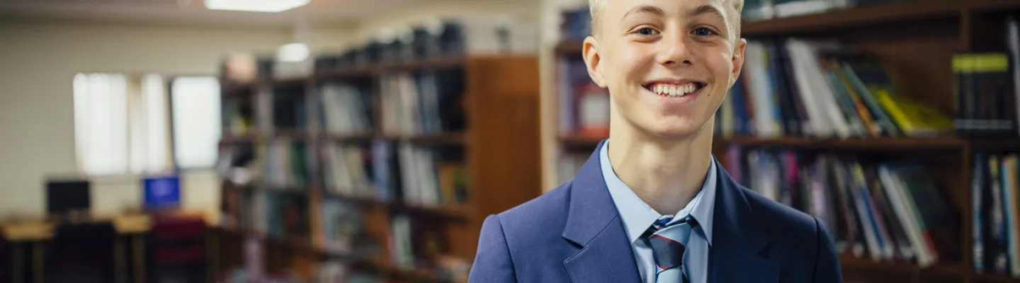 A young adult in school uniform standing next to library shelves
