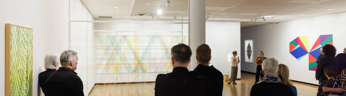 Photograph of gallery visitors looking several abstract artworks and installations.