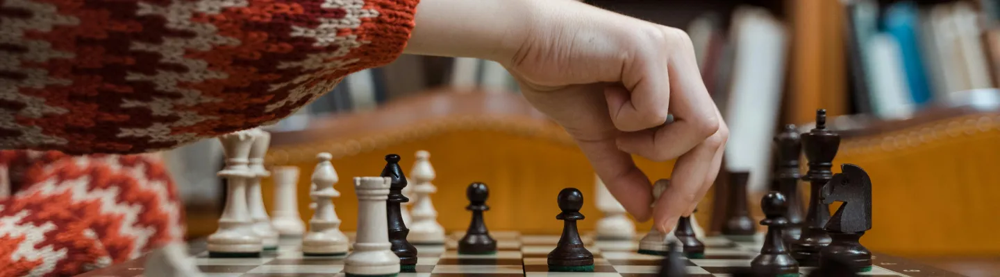 A person in a knitted sweater holding a chess piece over a chess board.