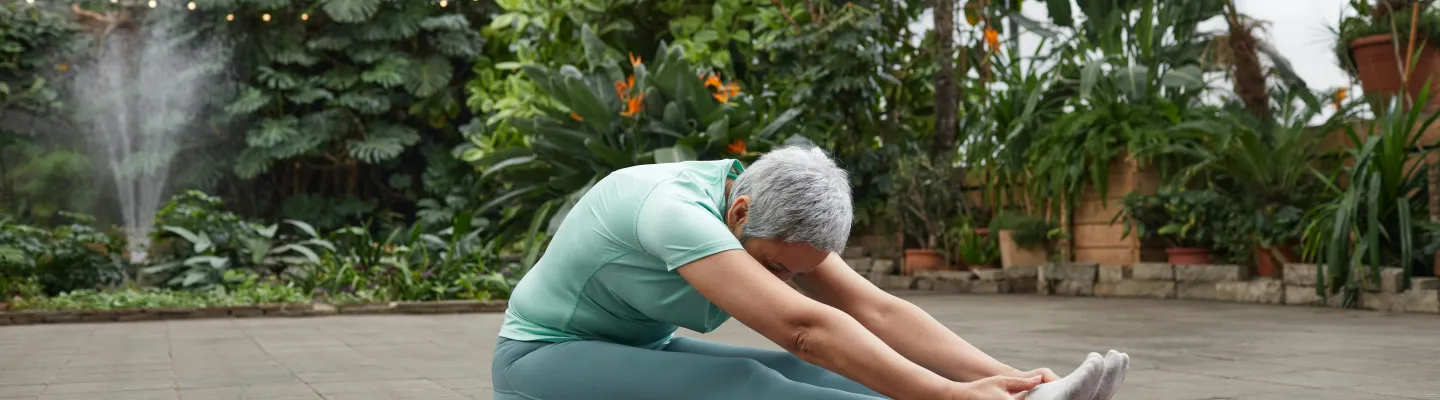 A woman has her legs out straight and is leaning forward to touch her toes.