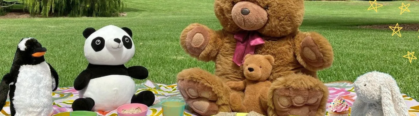 A group of teddys having a picnic. There is a penguin, a panda, a big brown bear and a rabbit.