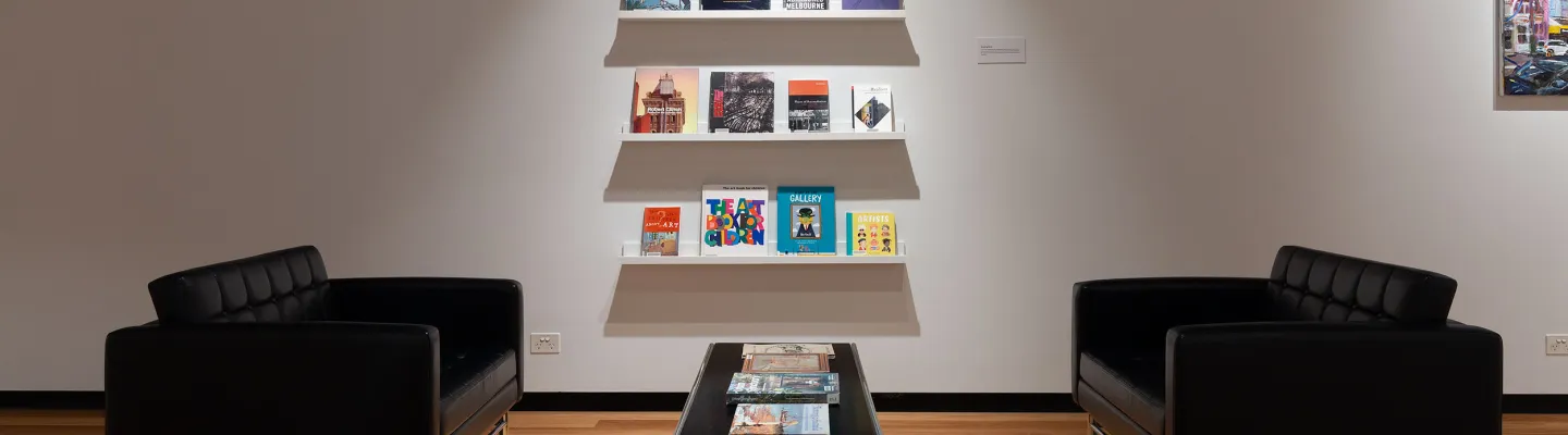 Shelves of art books displayed with tables and chairs within an art gallery.