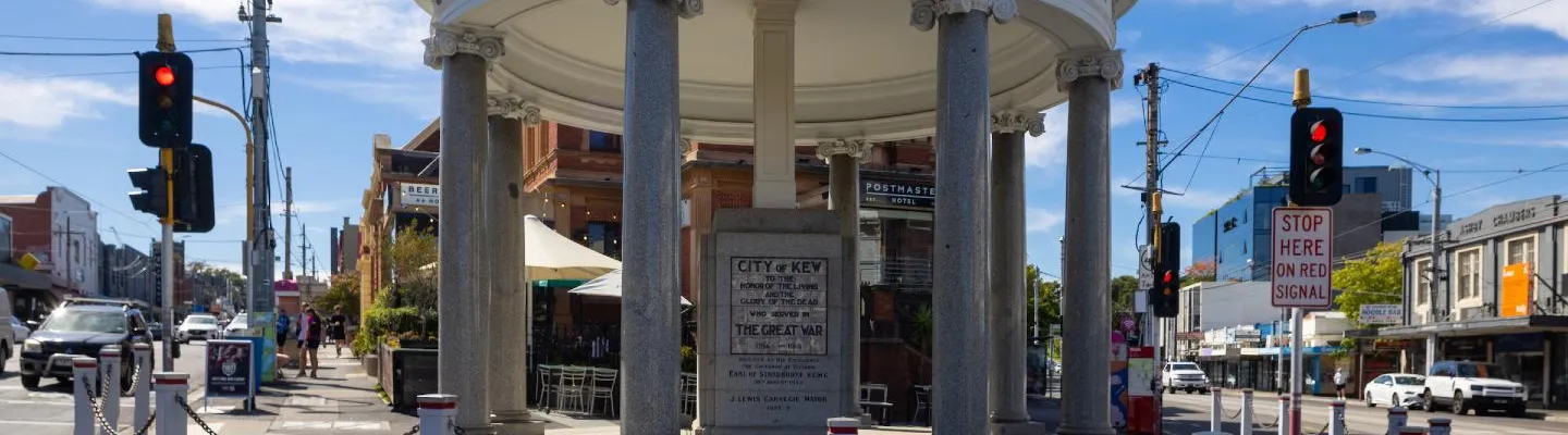 Street view of a cenotaph building on the edge of a roundabout with a historic building in background