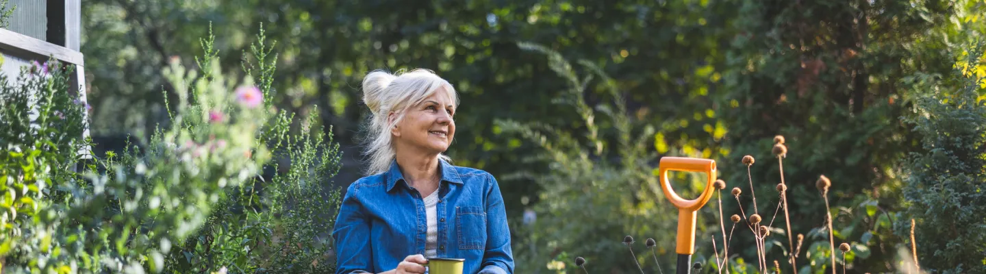 An older woman drinks a cup of tea in a bountiful garden