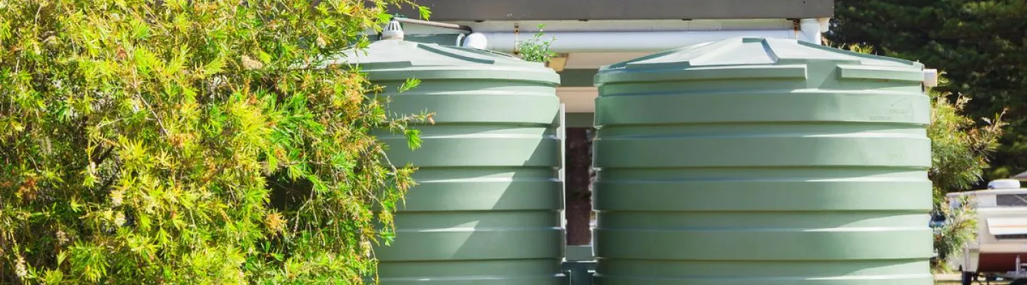 two large green water tanks near a house with solar panels on the roof.