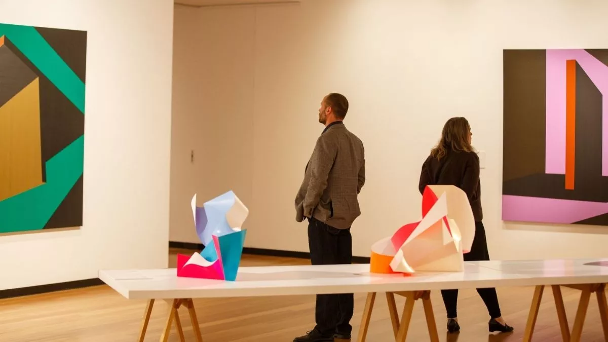 Visitors to 'Light Gestures' looking at paintings on the walls. In the foreground is a table with abstract sculptures. 