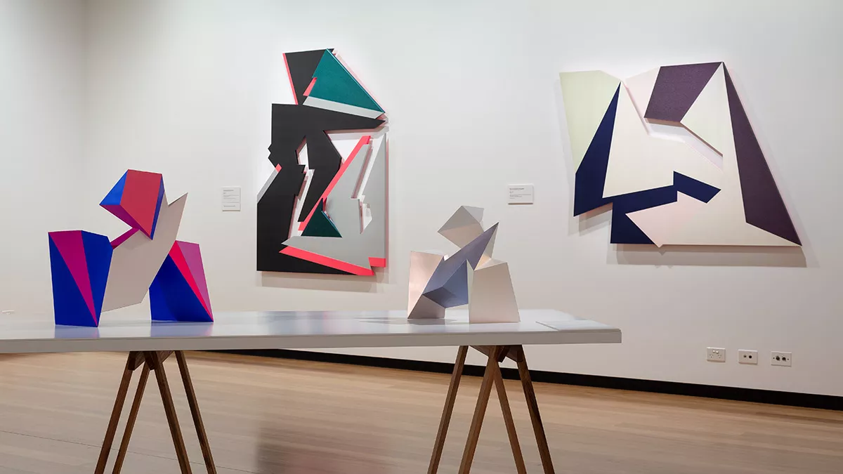 Installation view of 'Light Gestures' at Town Hall Gallery. Abstract geometric paintings on the wall made from cut out shapes. Abstract sculptures on a table, made up of large flat surfaces and lots of angles.
