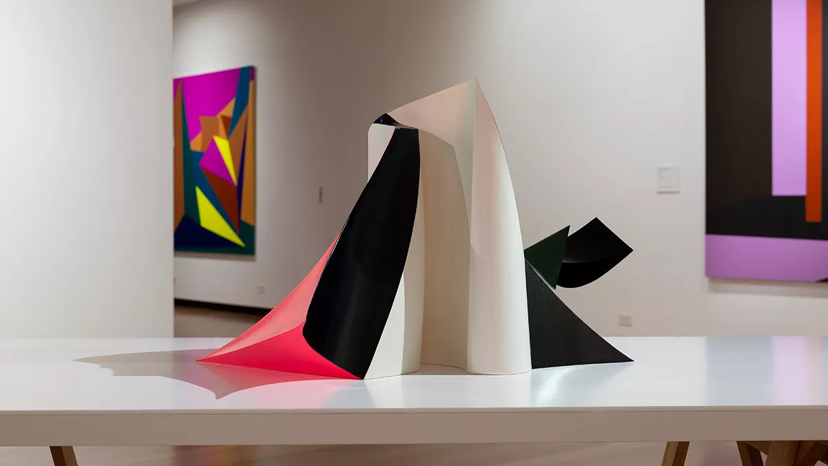Installation view of 'Light Gestures' at Town Hall Gallery. Abstract geometric paintings on the wall. Abstract sculpture on a table, made up of large flat surfaces and lots of angles.