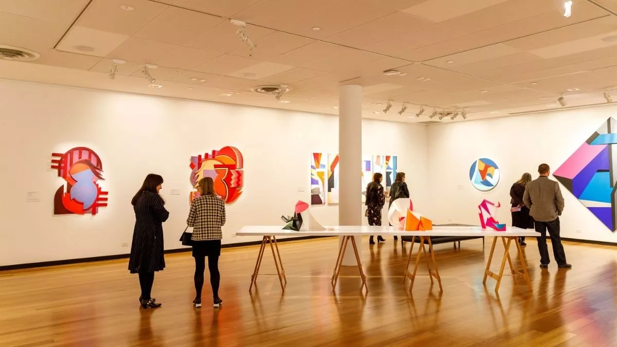 Visitors to 'Light Gestures' looking at paintings on the walls and sculptures on a table.
