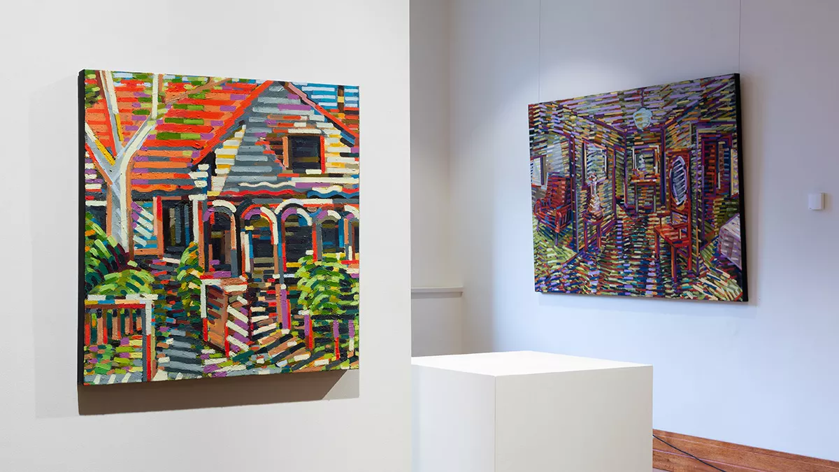 Painting on the section of wall on the left is of the exterior of a house, created out of lots of lines of colour. The painting on the right is of the interior of a hallway, with doorways on either side and ahead. In the hallway is a chair and a side table.