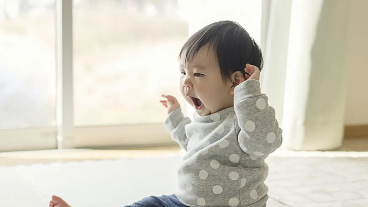 An older baby is sitting up and yawning