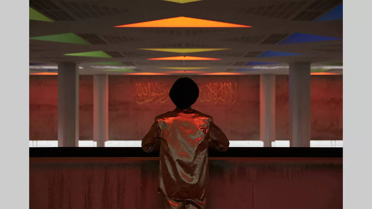 A figure with their back to us leaning on a barrier, looking out across an empty space that contains four pillars.